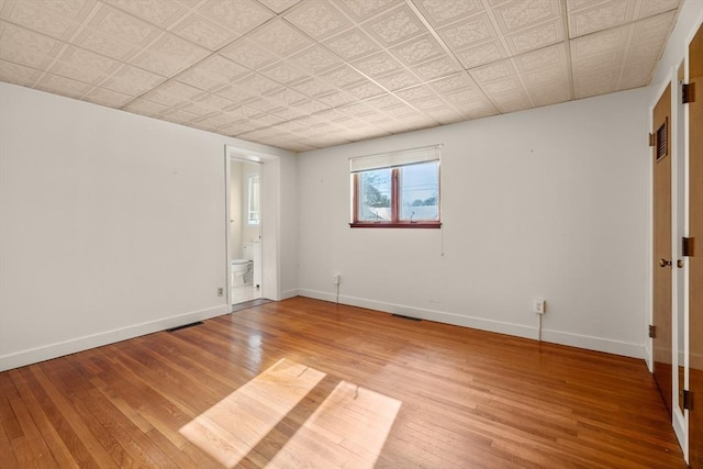 empty room featuring visible vents, light wood-type flooring, and baseboards