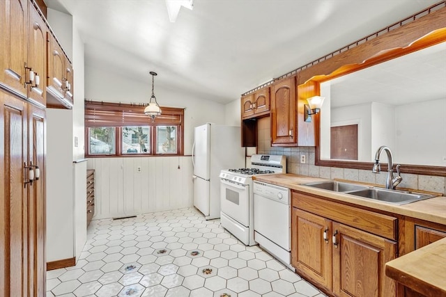 kitchen featuring a sink, white appliances, brown cabinetry, vaulted ceiling, and hanging light fixtures