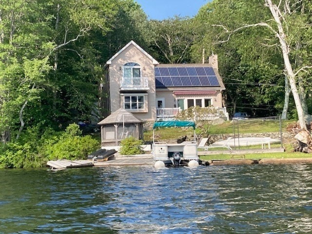 rear view of house featuring a balcony, a sunroom, a water view, and solar panels