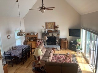 living room featuring ceiling fan, a fireplace, light hardwood / wood-style flooring, and high vaulted ceiling