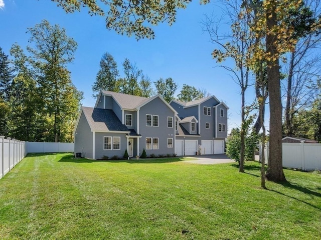 rear view of property with an attached garage, driveway, fence, and a lawn