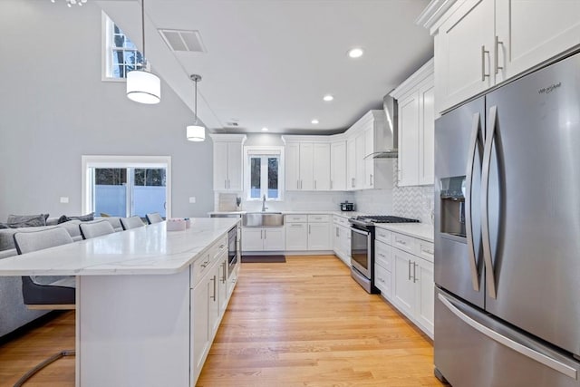 kitchen with appliances with stainless steel finishes, light wood-style flooring, wall chimney exhaust hood, decorative backsplash, and a sink