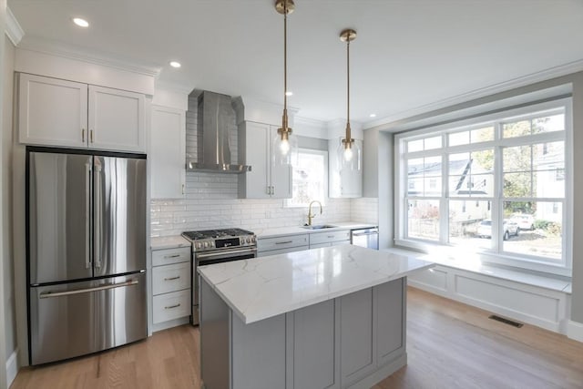 kitchen featuring a center island, appliances with stainless steel finishes, wall chimney range hood, pendant lighting, and light stone counters