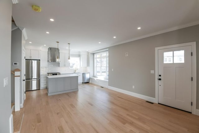 kitchen featuring wall chimney range hood, a kitchen island, white cabinets, pendant lighting, and stainless steel appliances