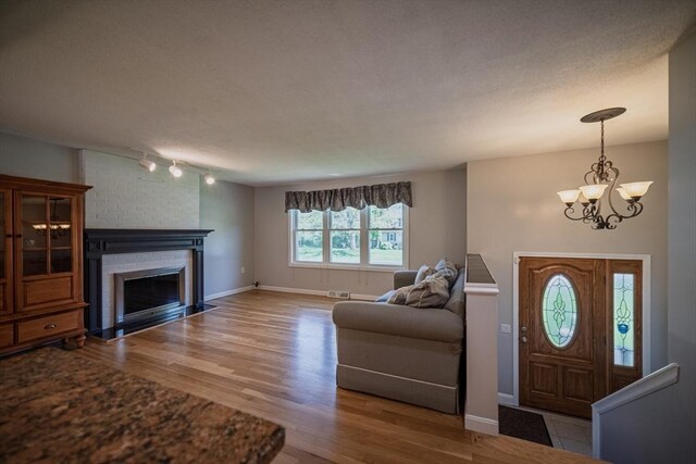 foyer with a chandelier, wood finished floors, a brick fireplace, and baseboards