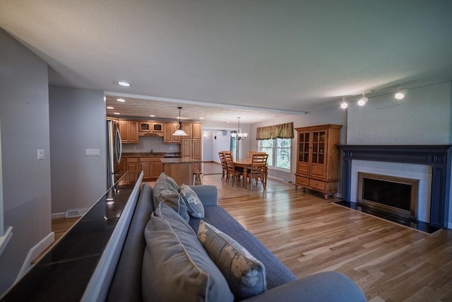 living room featuring light wood finished floors, a chandelier, a brick fireplace, baseboards, and recessed lighting