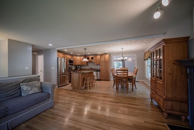 living area featuring light wood-style flooring, a textured ceiling, a chandelier, recessed lighting, and baseboards
