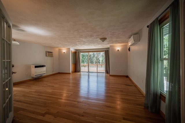 unfurnished living room with heating unit, an AC wall unit, wood finished floors, and baseboards