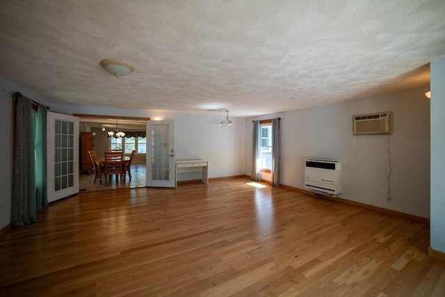 unfurnished living room with a chandelier, heating unit, baseboards, light wood finished floors, and a textured ceiling