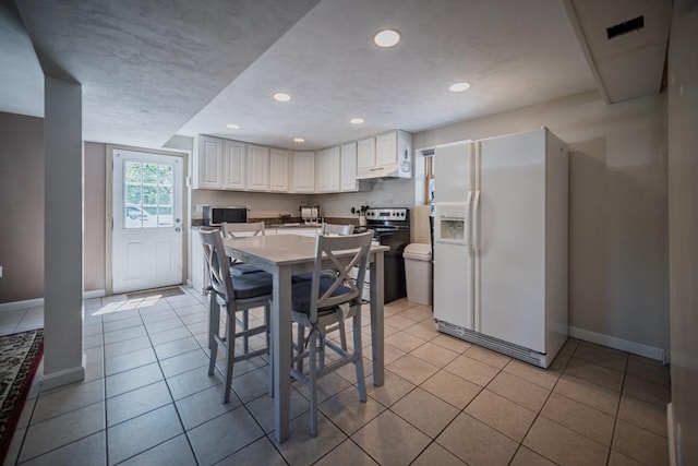 kitchen featuring white refrigerator with ice dispenser, stainless steel microwave, electric range oven, baseboards, and light tile patterned floors