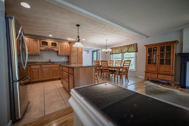 kitchen featuring freestanding refrigerator, a sink, glass insert cabinets, a kitchen island, and a chandelier