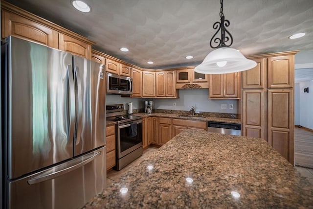 kitchen with appliances with stainless steel finishes, a sink, recessed lighting, dark stone counters, and pendant lighting