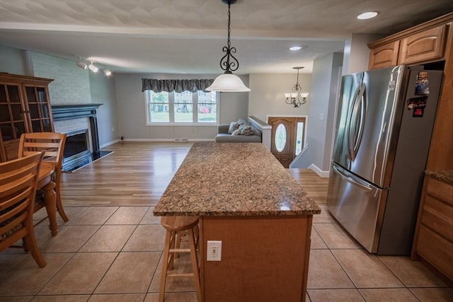 kitchen with freestanding refrigerator, a fireplace, light tile patterned floors, open floor plan, and a center island