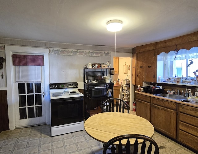 kitchen with white electric range oven, hanging light fixtures, and sink