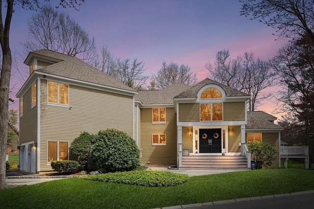 view of front facade with a shingled roof, an attached garage, and a front yard