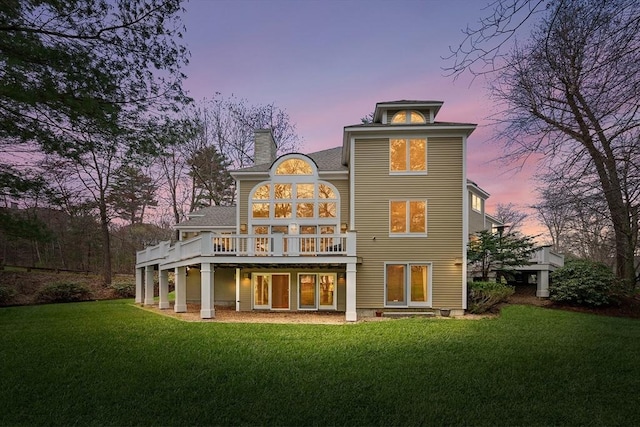 back of house at dusk featuring a chimney, a yard, and a deck