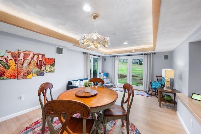 dining space with visible vents, baseboards, light wood-style floors, a raised ceiling, and a chandelier