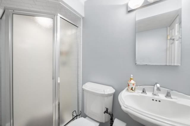 bathroom with a sink, a stall shower, and toilet