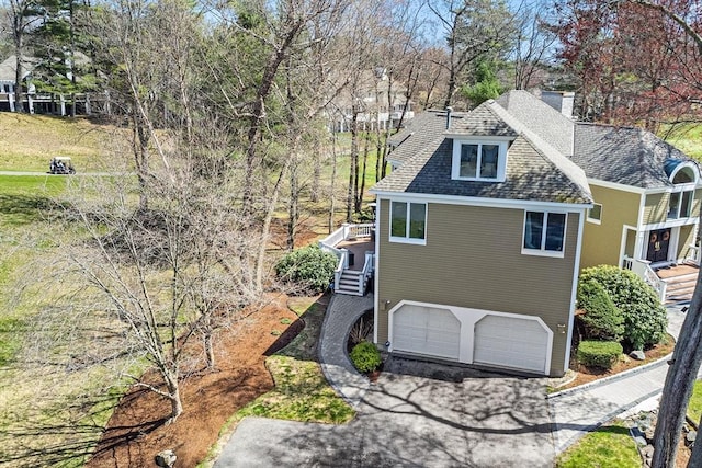 exterior space featuring a chimney, roof with shingles, aphalt driveway, an attached garage, and stairs