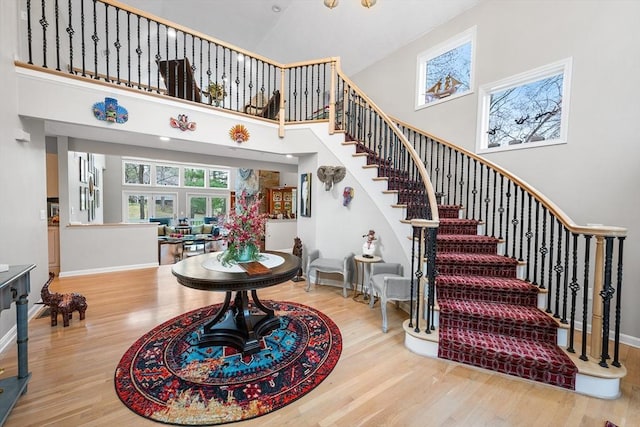 stairway with baseboards, wood finished floors, and a towering ceiling