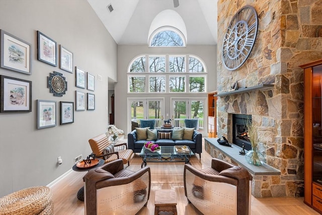 living area with high vaulted ceiling, plenty of natural light, a stone fireplace, and wood finished floors