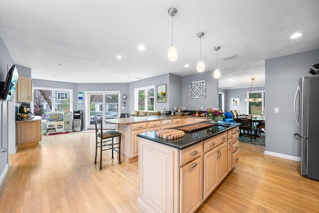 kitchen featuring a center island, freestanding refrigerator, light wood finished floors, and a breakfast bar