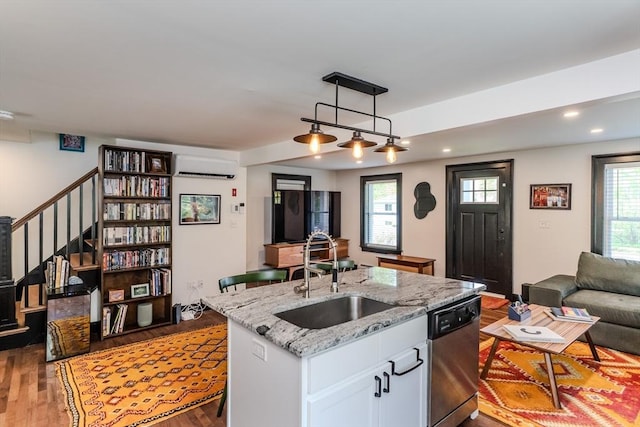 kitchen with stainless steel dishwasher, a sink, a wall mounted AC, open floor plan, and wood finished floors