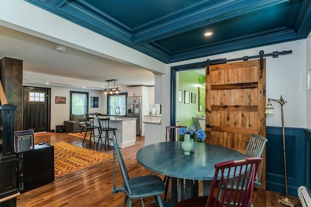 dining room featuring a barn door, crown molding, wood finished floors, and a baseboard heating unit