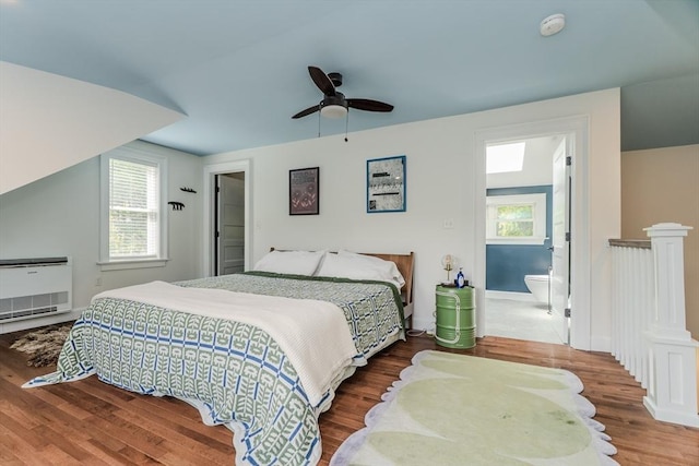 bedroom featuring wood finished floors, multiple windows, heating unit, and a ceiling fan