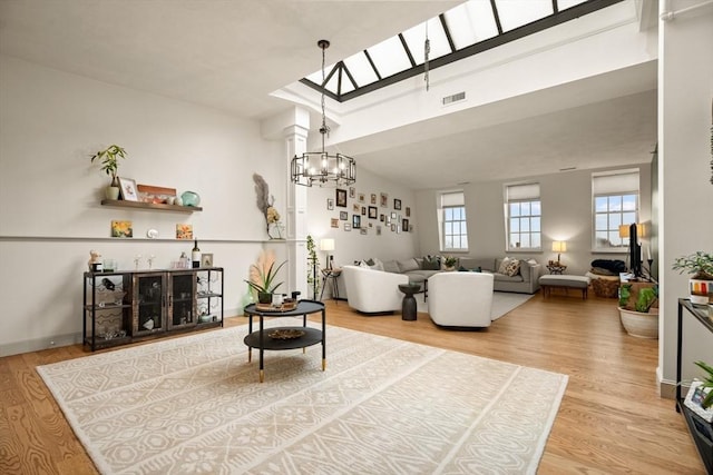 living area with visible vents, an inviting chandelier, wood finished floors, vaulted ceiling with skylight, and baseboards