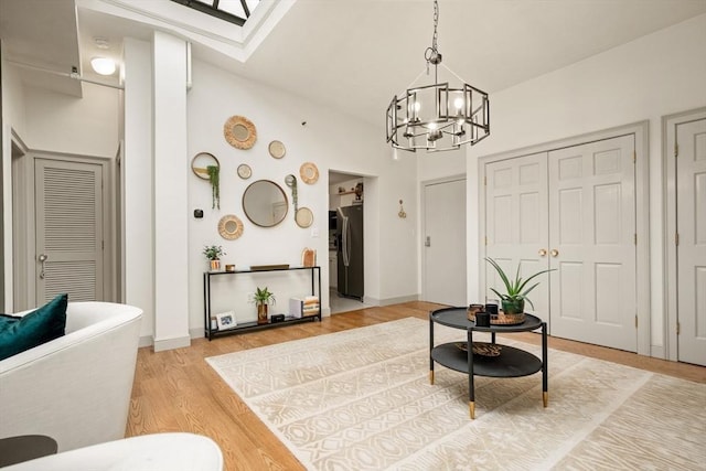 sitting room with light wood-type flooring, a skylight, a notable chandelier, and baseboards