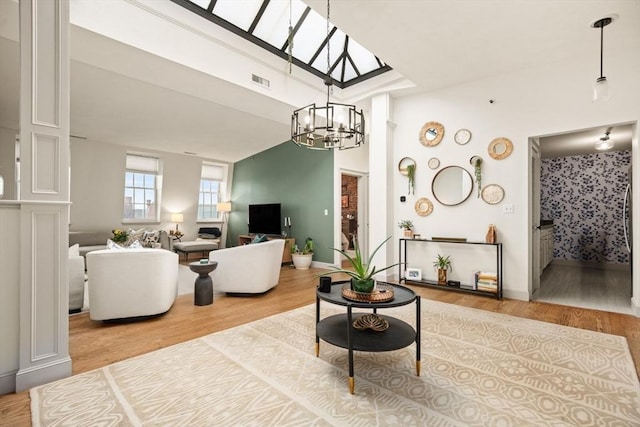 living area with a chandelier, wood finished floors, visible vents, baseboards, and lofted ceiling with skylight