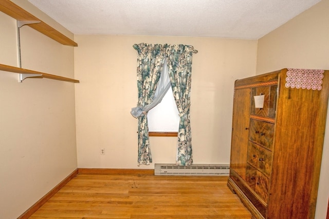 unfurnished room featuring baseboard heating, a textured ceiling, and light hardwood / wood-style flooring