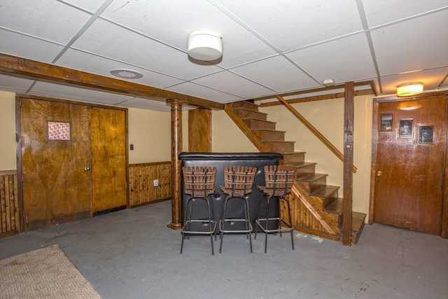 bar featuring concrete floors, wooden walls, and a drop ceiling