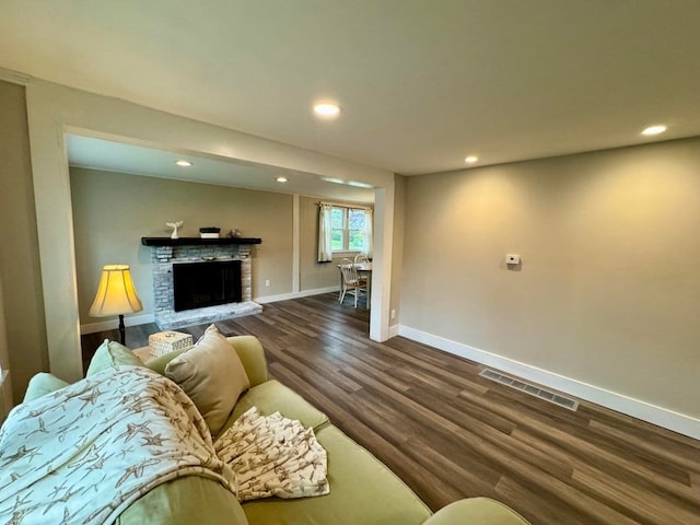 living room featuring a stone fireplace and dark hardwood / wood-style flooring