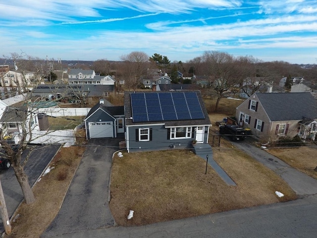 view of front facade featuring solar panels, an attached garage, a front yard, a residential view, and driveway