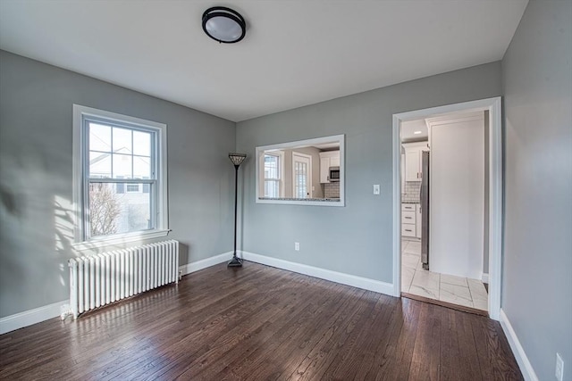 unfurnished bedroom with dark wood-style floors, radiator heating unit, and baseboards