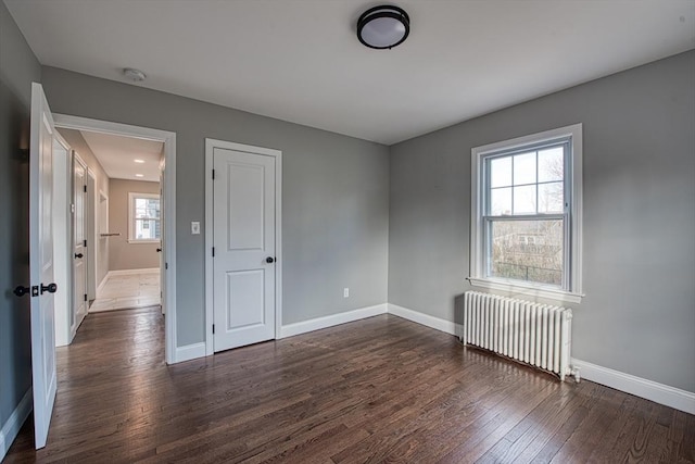 empty room featuring dark wood-style flooring, baseboards, and radiator heating unit