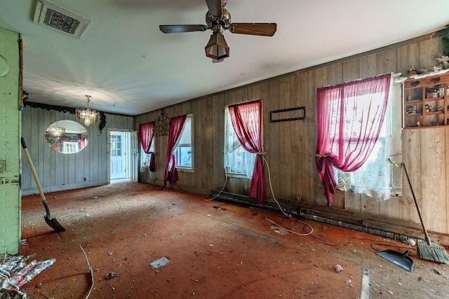 interior space with ceiling fan with notable chandelier, plenty of natural light, and wooden walls