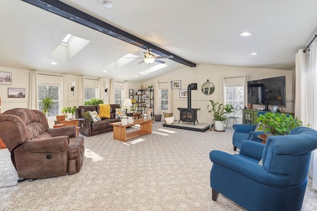 living room with ceiling fan, a wood stove, vaulted ceiling with skylight, and carpet flooring