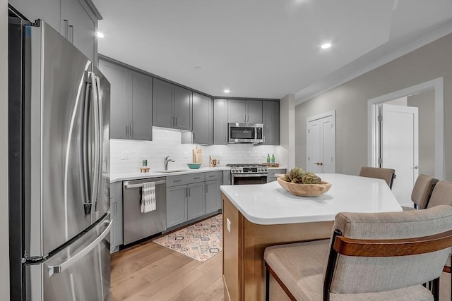 kitchen with light wood-style floors, gray cabinets, appliances with stainless steel finishes, a sink, and a breakfast bar area