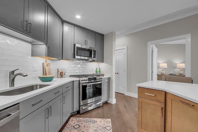 kitchen featuring tasteful backsplash, a sink, light countertops, appliances with stainless steel finishes, and light wood-style flooring