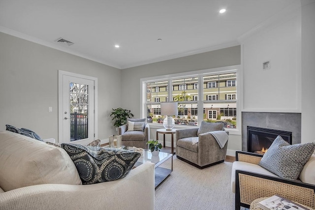 living area featuring a glass covered fireplace, recessed lighting, visible vents, and ornamental molding