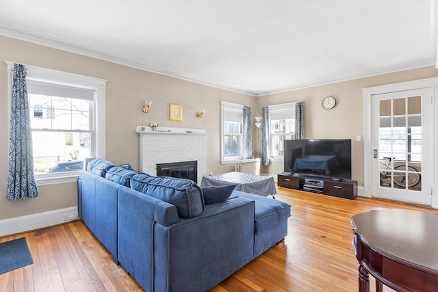 living room featuring light wood-style floors, baseboards, a brick fireplace, and ornamental molding