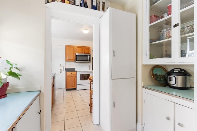 kitchen with white range with electric stovetop, light tile patterned floors, light countertops, stainless steel microwave, and glass insert cabinets