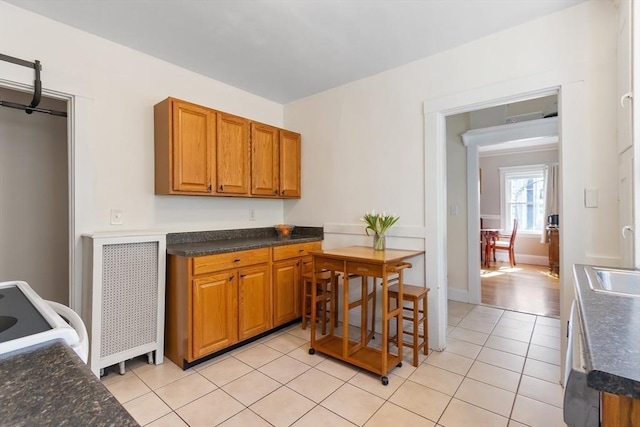 kitchen featuring light tile patterned floors, baseboards, electric stove, brown cabinets, and a sink