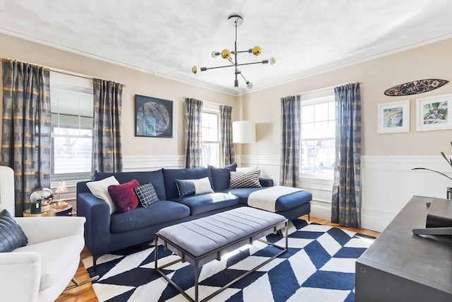 living room featuring wainscoting, a healthy amount of sunlight, crown molding, and an inviting chandelier