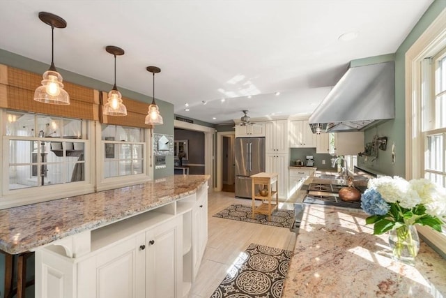 kitchen featuring pendant lighting, stainless steel refrigerator, a sink, light stone counters, and exhaust hood