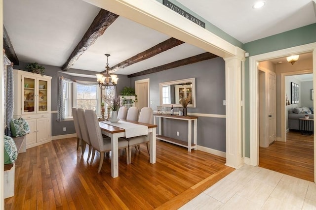 dining space with beamed ceiling, a notable chandelier, light wood finished floors, baseboards, and ornate columns