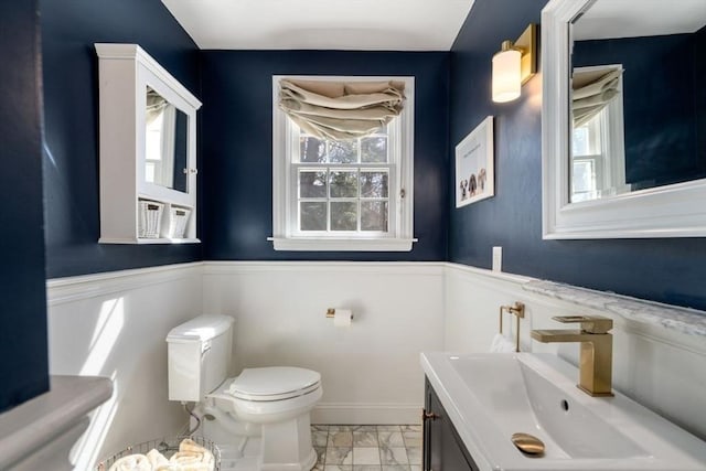 bathroom featuring vanity, toilet, marble finish floor, and wainscoting